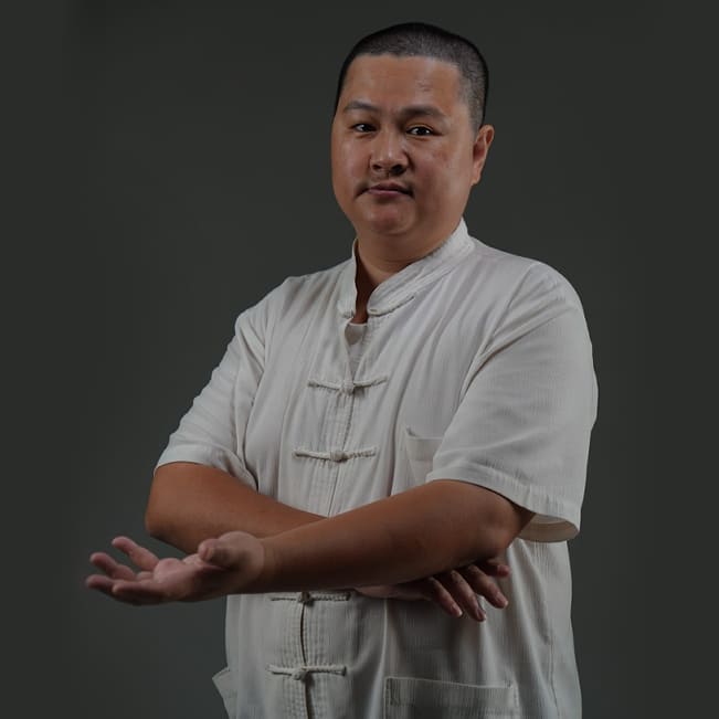 順周堂專業調理師傅形象照，身穿白色傳統盤扣唐裝，面色和善、伸出一隻手，展現專業且親切的職人精神。建立客戶對師傅的專業信任感。